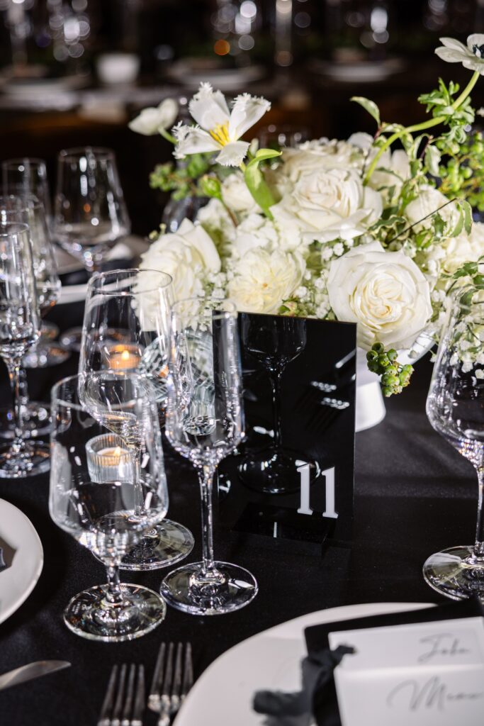 Elegant table setting with white floral centerpiece, glassware, and a black table number card displaying the number 11.