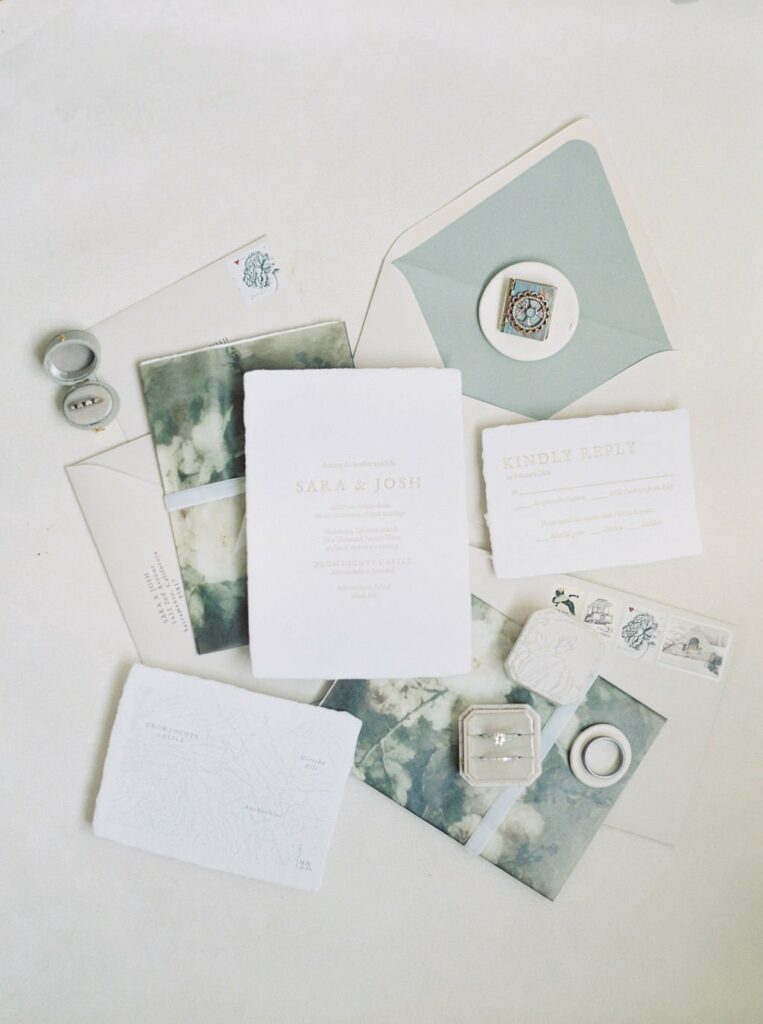A collection of wedding invitations and stationery featuring muted sea green and white colors, including an RSVP card, envelopes, and a wax seal.