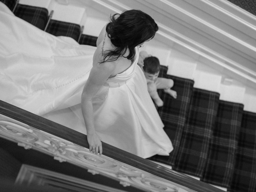 A woman in a white dress descends a staircase, with a child sitting on the steps below her, as seen from above.
