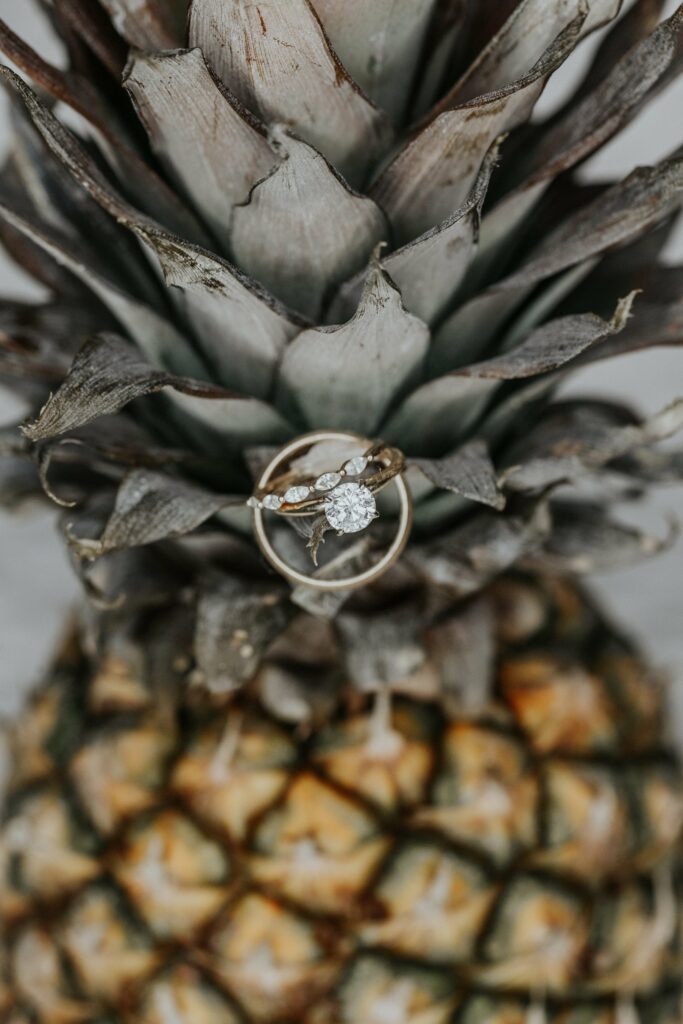 A diamond engagement ring with a twisted band is placed on the rough exterior of a pineapple.
