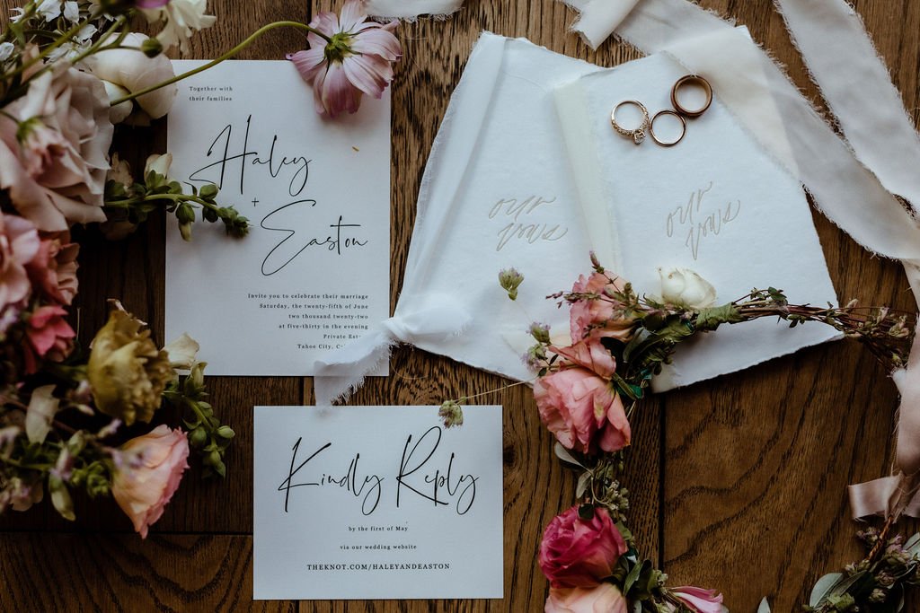 Wedding invitations and reply cards adorned with floral arrangements and three rings on a wooden surface. The name "Haley Easton" is printed on the invitations.