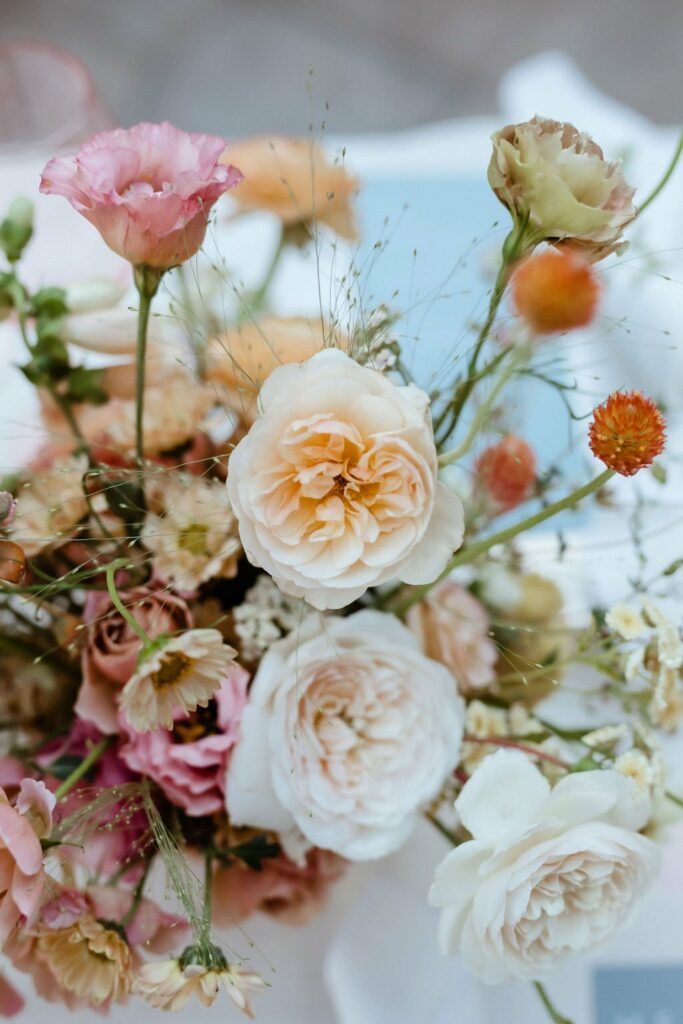 A close-up of a floral arrangement featuring pink and white roses, carnations, and smaller orange and white flowers with green stems and leaves.