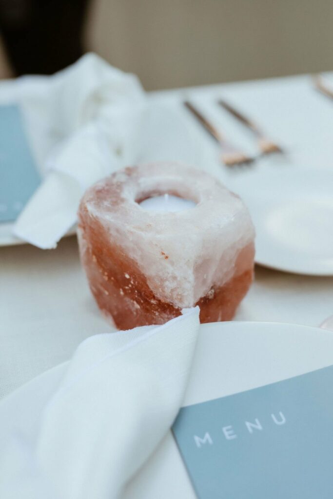 A napkin and menu are placed on a plate beside a salt candle holder on a set dining table with silverware.