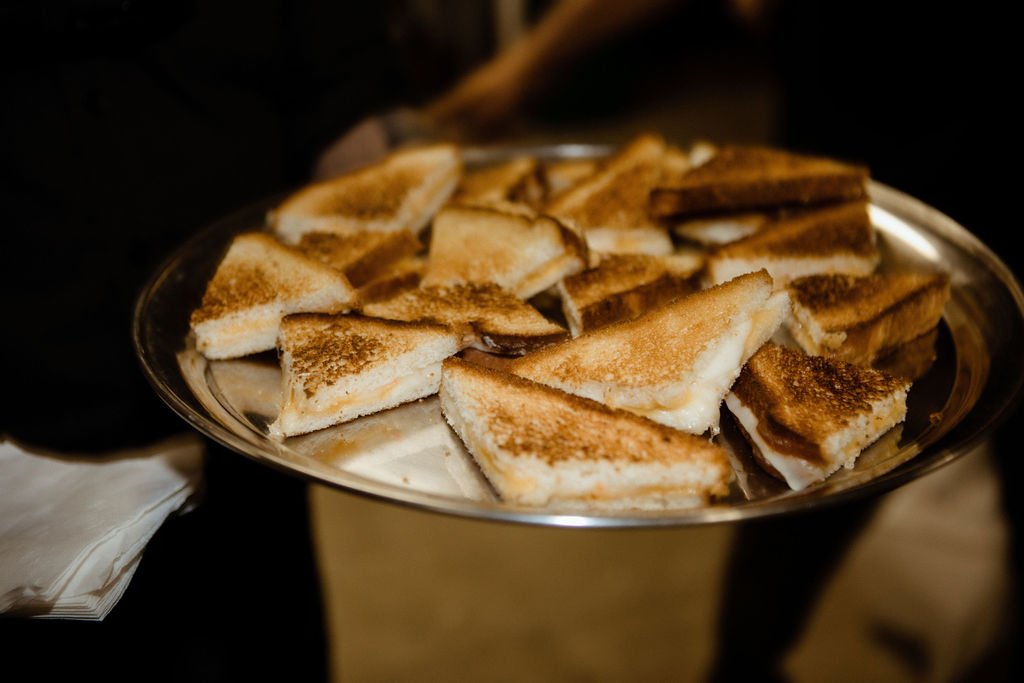 A metal tray filled with multiple toasted sandwich triangles, each containing melted cheese.