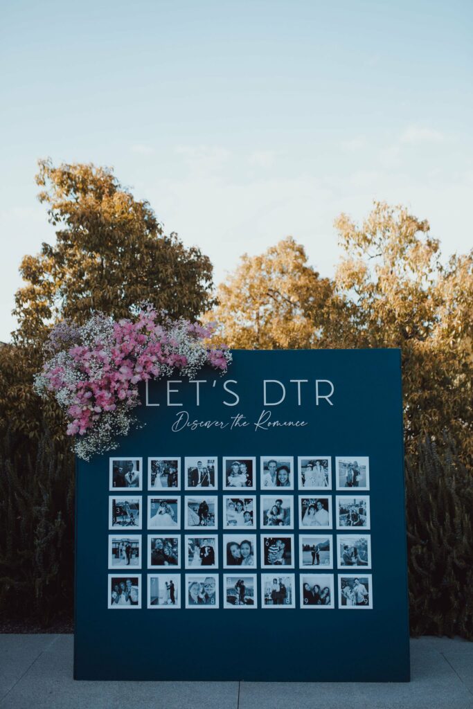 A large display with "Let's DTR Discover the Romance" at the top, decorated with pink flowers and featuring numerous black-and-white photos of couples against a backdrop of trees.