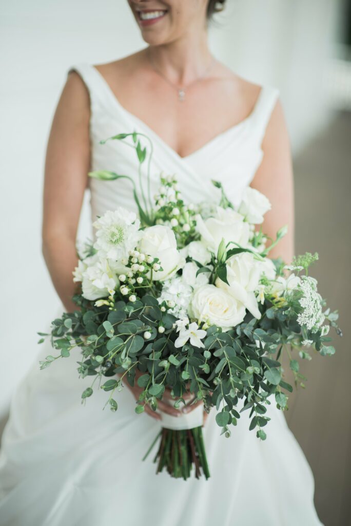 A bride in a white dress holding a large bouquet of white flowers and green eucalyptus leaves.