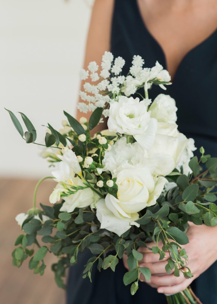 A person in a dark dress holds a bouquet of white flowers and green foliage.