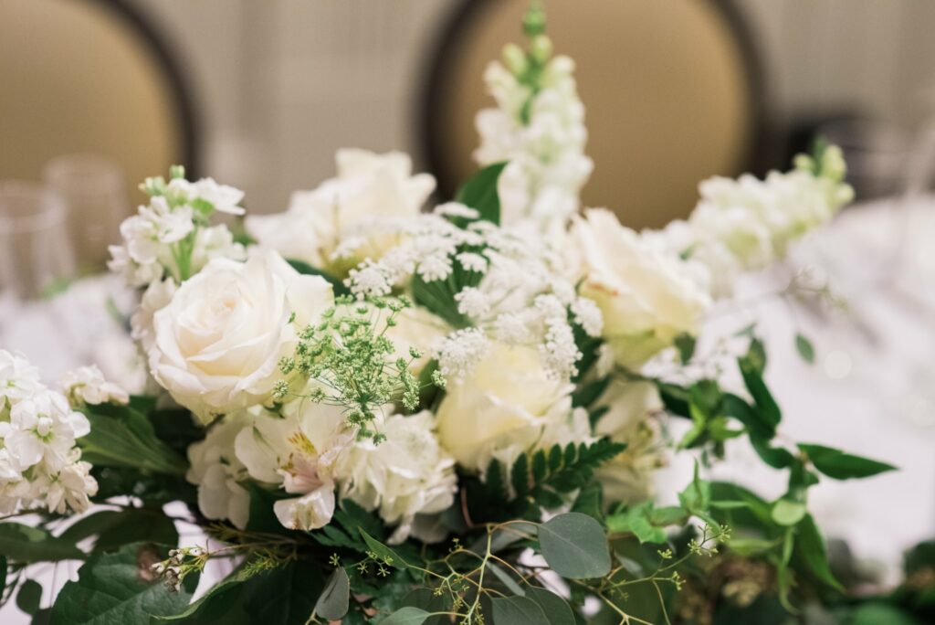 A floral arrangement featuring white roses, snapdragons, and greenery on a table with a blurred background.