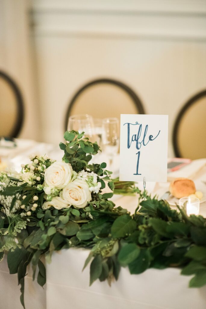 A table decorated with white flowers, leafy greenery, and candles displays a sign that reads "Table 1.