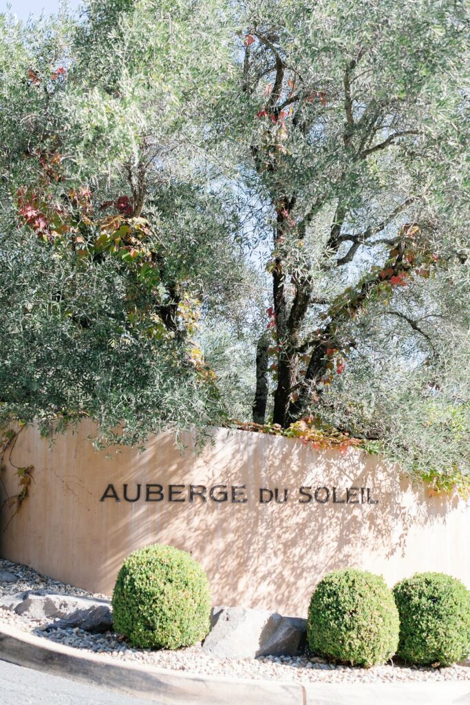 Entrance sign for Auberge du Soleil, featuring neatly trimmed bushes and lush trees.