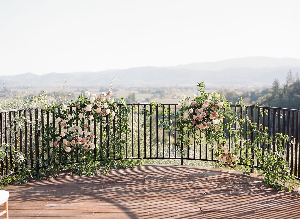 An outdoor balcony adorned with floral arrangements overlooks a scenic landscape with hills in the background.