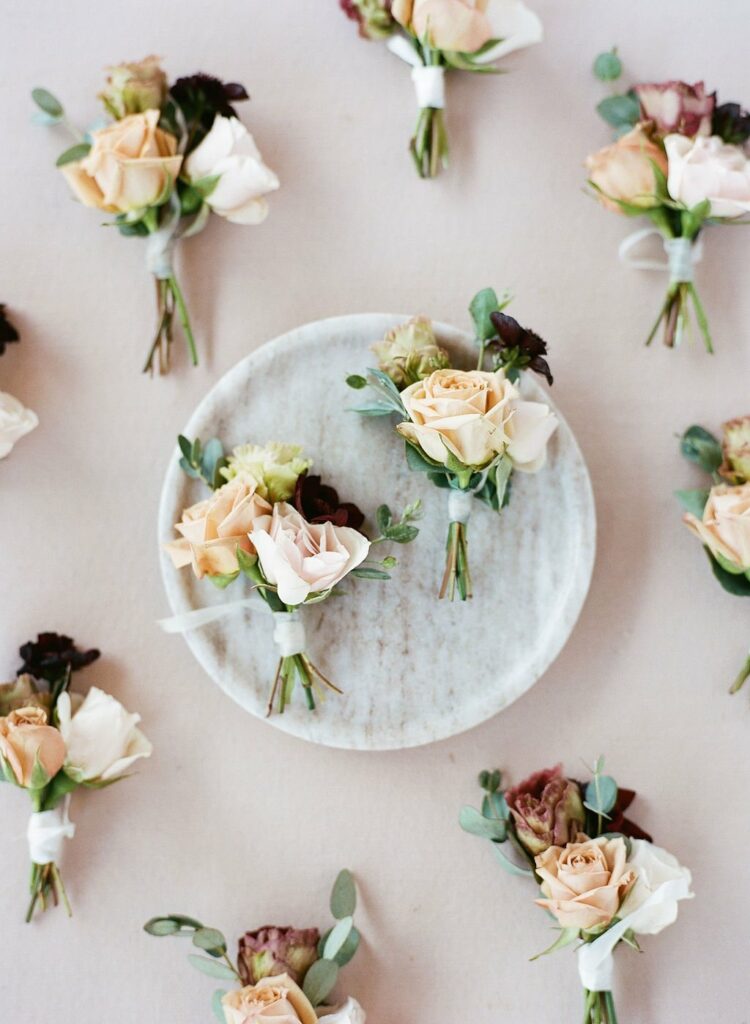 A white plate with small bouquets of pastel roses and greenery, surrounded by similar bouquets arranged on a light-colored surface.