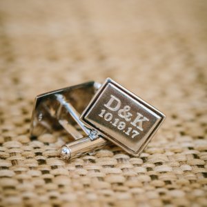 A pair of cufflinks on a woven surface with "D&K 10.18.17" engraved on them.