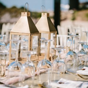 A table setting featuring two decorative lanterns surrounded by upside-down wine glasses and place settings with rolled napkins.