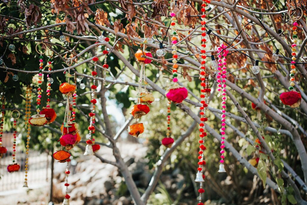 Colorful decorations, including flowers and beads, hang from tree branches in an outdoor setting.