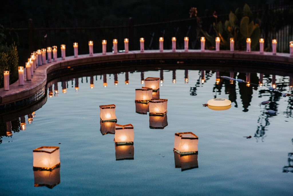 A swimming pool is decorated with floating lanterns and surrounded by lit candles in a nighttime setting.