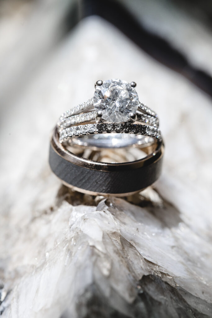 A diamond engagement ring and a wedding band are positioned on a textured surface.