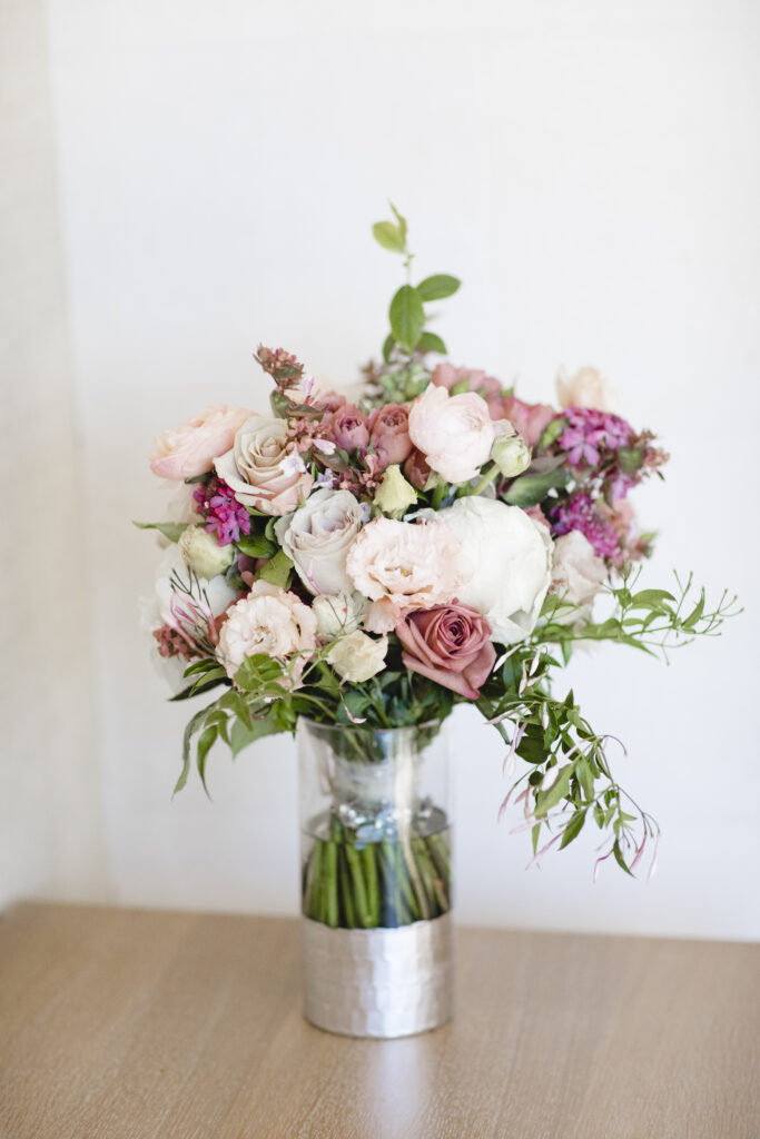 A bouquet of pink and white roses with green leaves in a clear vase on a wooden surface.