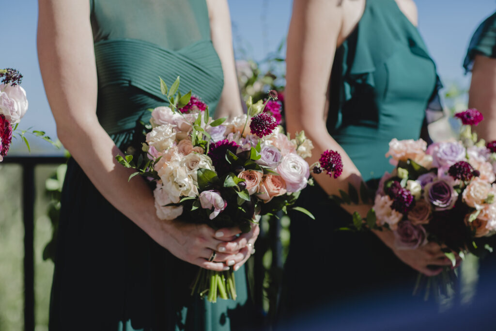 Three people wearing green dresses holding colorful bouquets with pink, white, and burgundy flowers.
