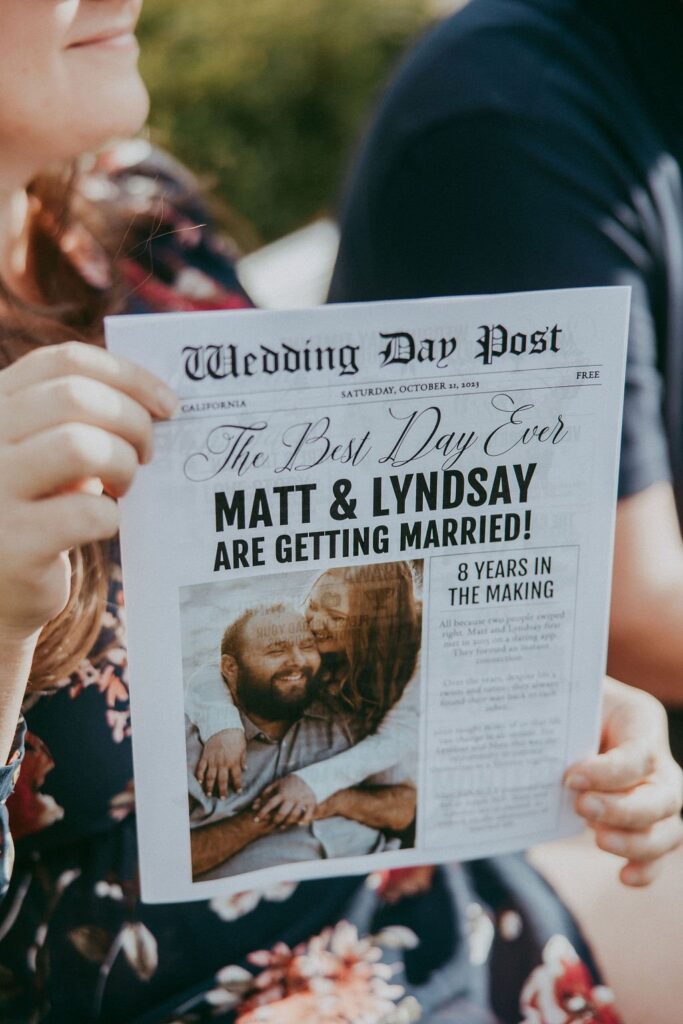 Person holding a newspaper-style wedding announcement for Matt and Lyndsay, titled "The Best Day Ever," with a description of 8 years together.