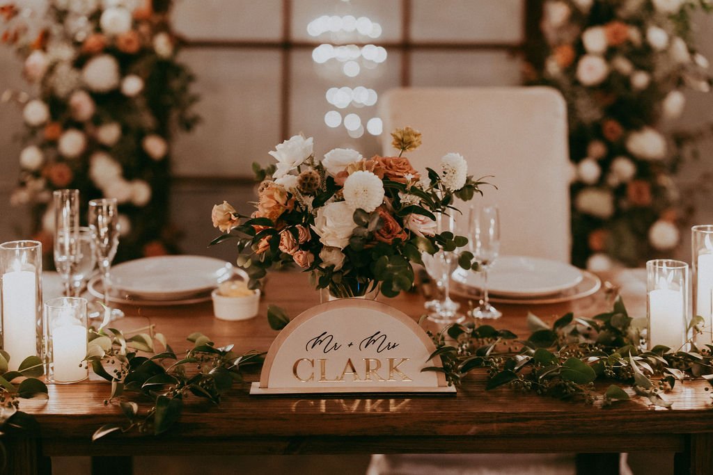 Elegant wedding table setting with a floral centerpiece, candles, plates, and a "Mr. & Mrs. Clark" sign.