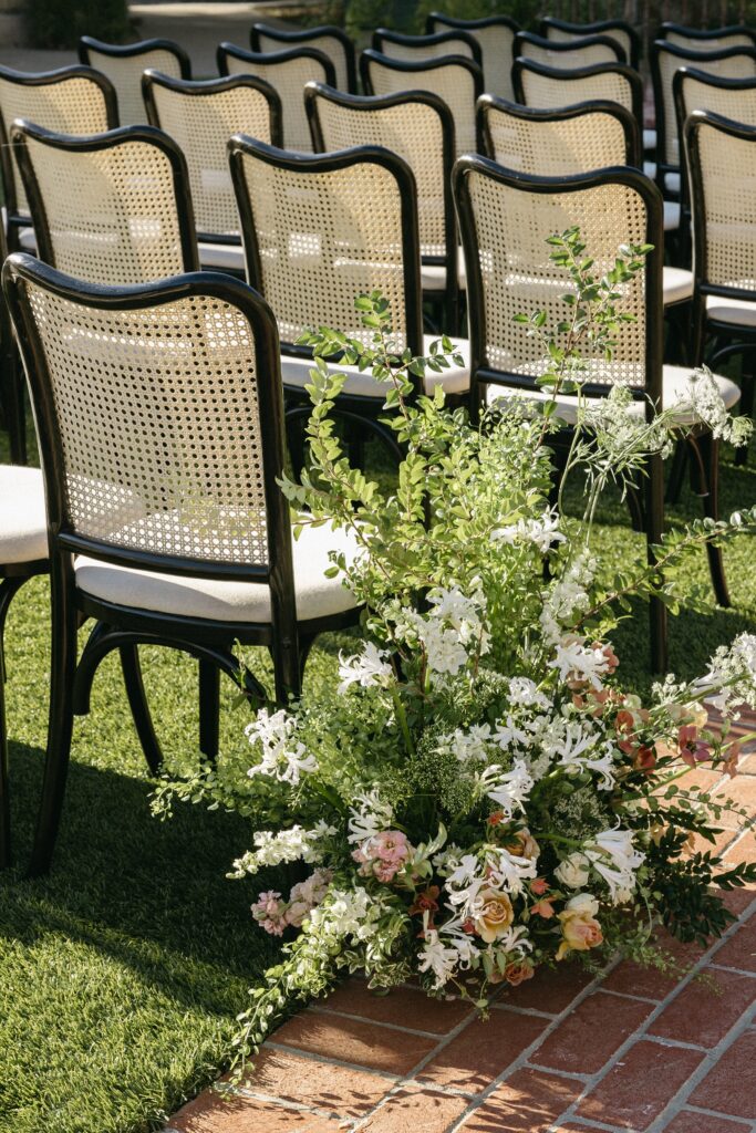 Rows of black chairs on a grass aisle with a floral arrangement of white and pink flowers at the front.