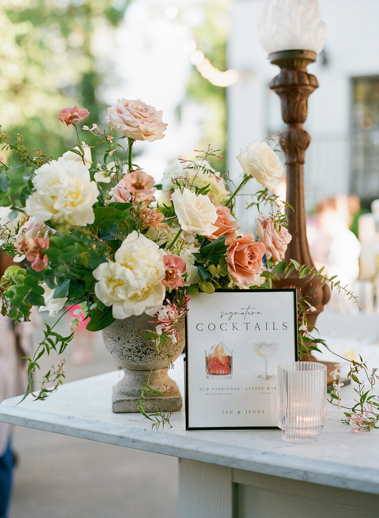 A delicate floral arrangement graces the table beside a cocktail menu, with a glass of water shimmering in the outdoor setting, capturing the enchanting essence of Park Winters weddings.