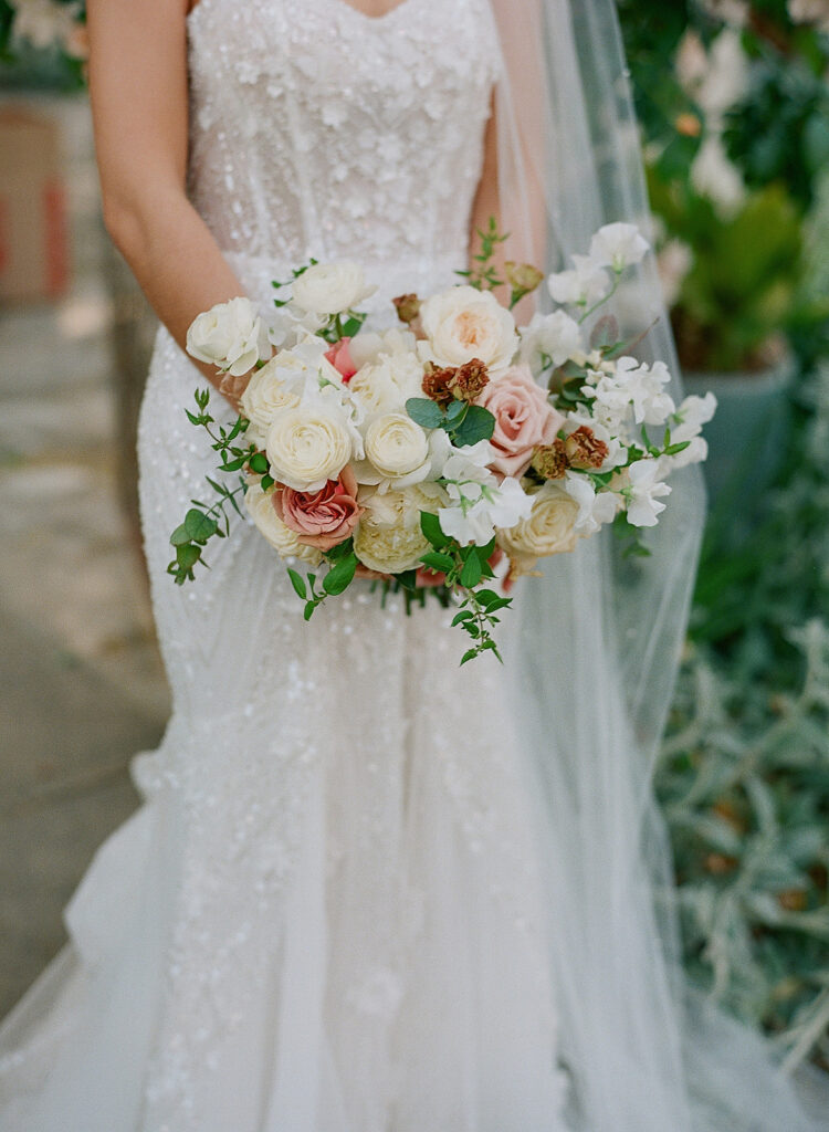 At Park Winters Weddings, a bride in a white lace dress gracefully holds a bouquet of white, pink, and peach flowers.