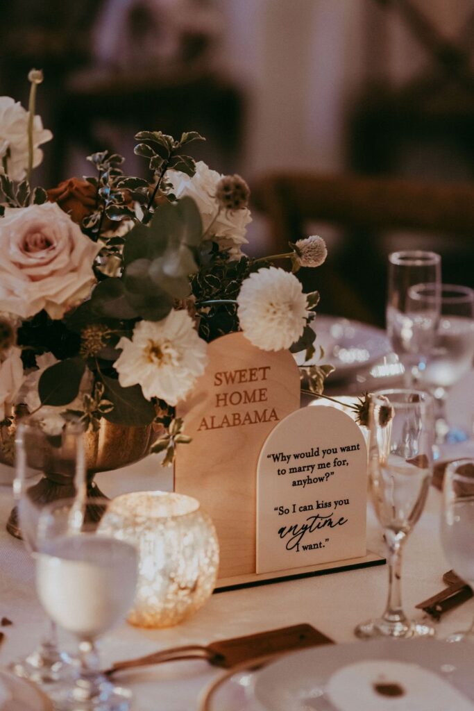 Table with floral centerpiece, engraved wooden signs with quotes, candles, and glassware.