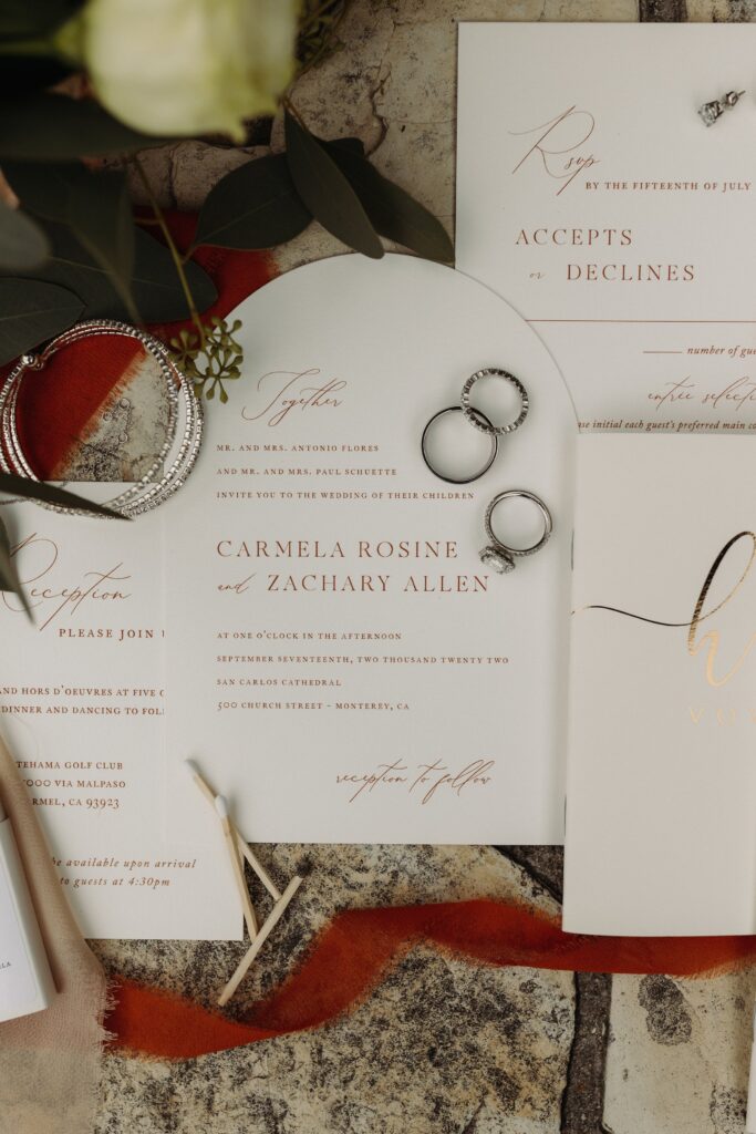 Wedding invitation set with RSVP card, two rings, and an envelope, displayed on a textured surface. Invitation for Carmela Rosine and Zachary Allen at Catalina Golf Club.