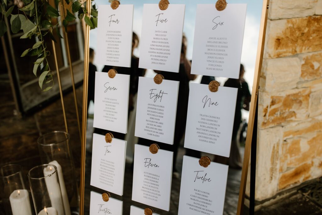 Wedding seating chart on a mirror with wax seals, surrounded by candles and greenery.
