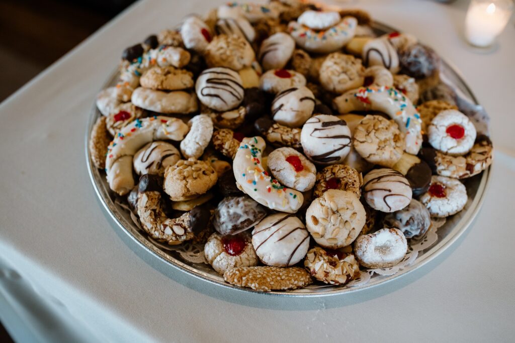 A platter filled with a variety of cookies, including ones with chocolate drizzle, powdered sugar, and colorful sprinkles, displayed on a white tablecloth.