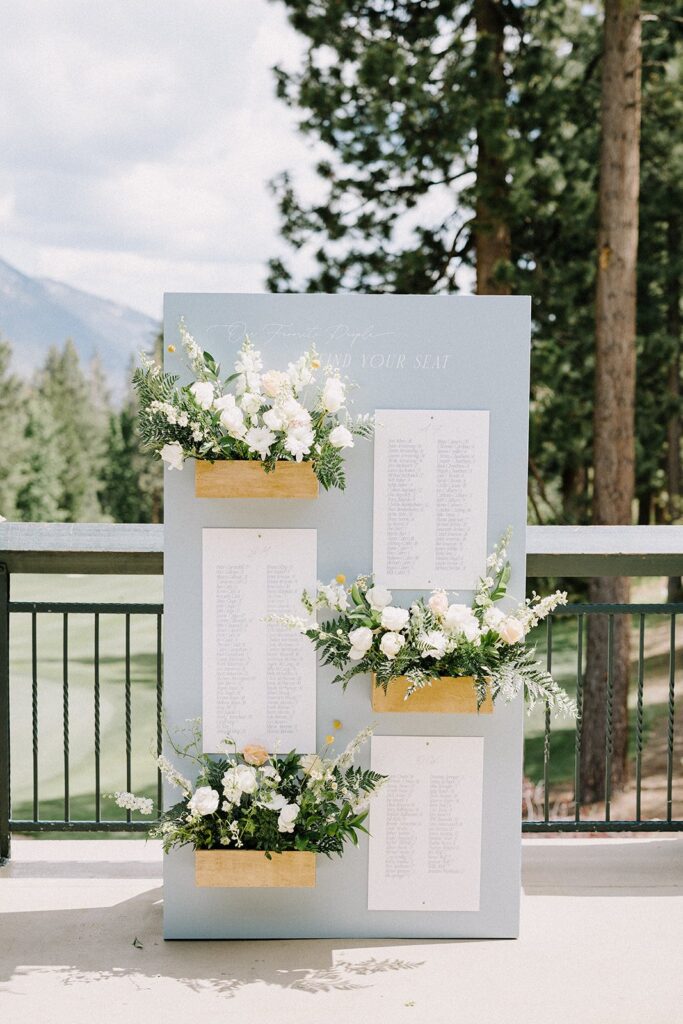 Wedding seating chart displayed outdoors with floral arrangements and a backdrop of trees and mountains.
