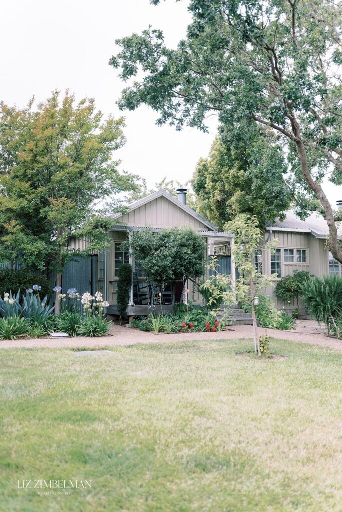 A quaint house with a front porch is surrounded by lush greenery and trees.