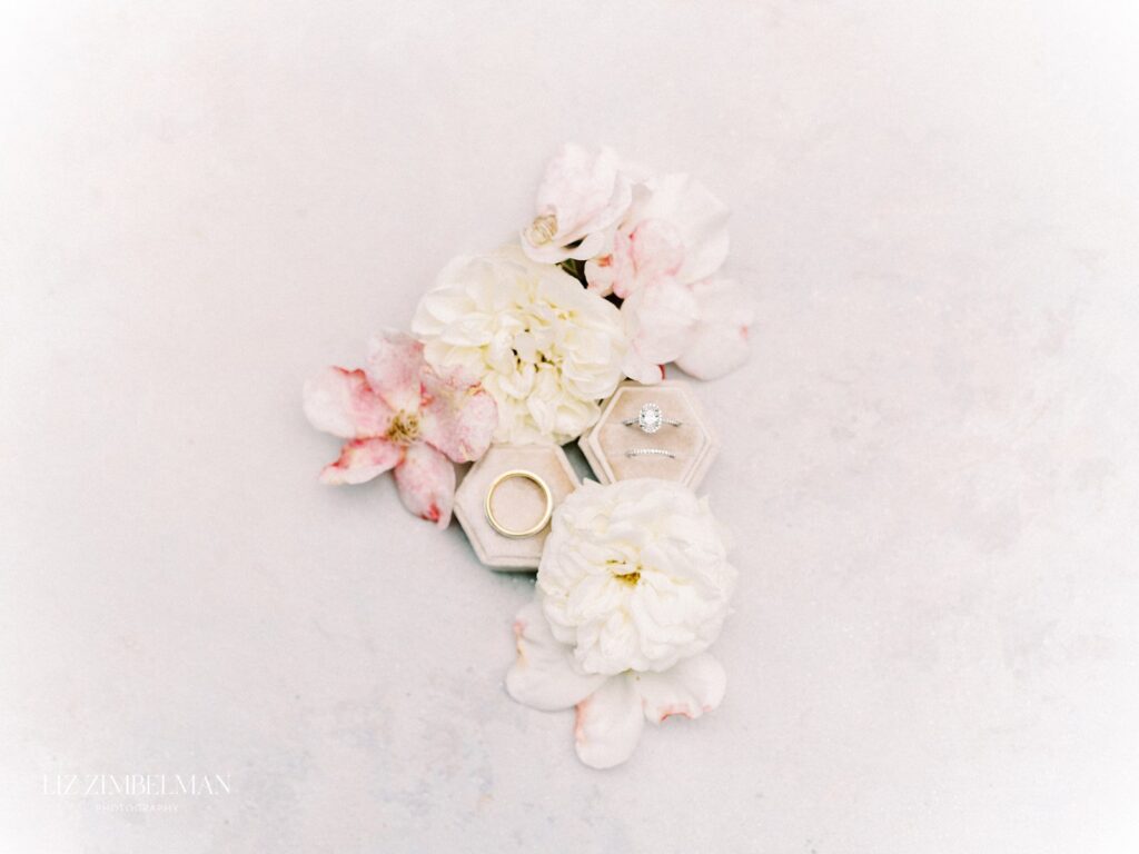Rings in hexagonal boxes surrounded by white and pink flowers on a light background.