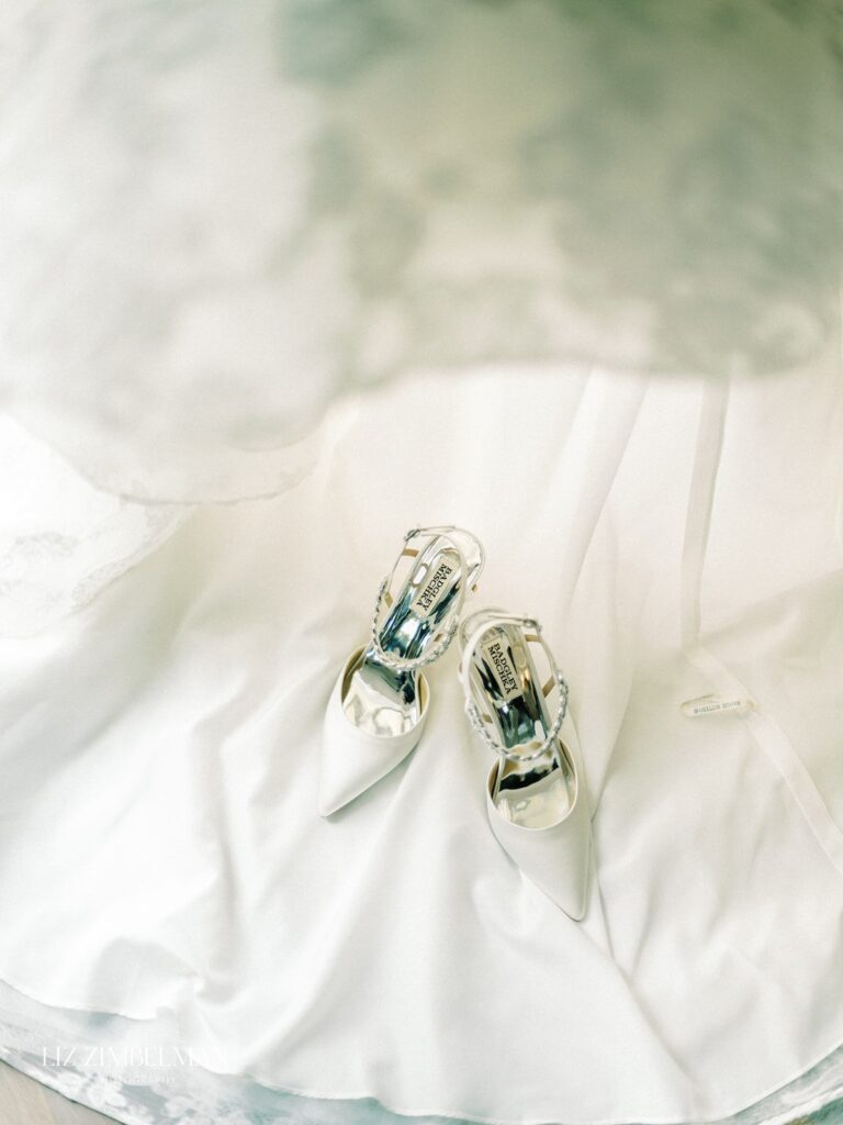 White high-heeled shoes adorned with shiny embellishments placed on a white fabric background.