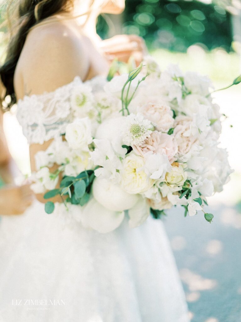 Bride in a white lace dress holding a bouquet of white and pale pink flowers.