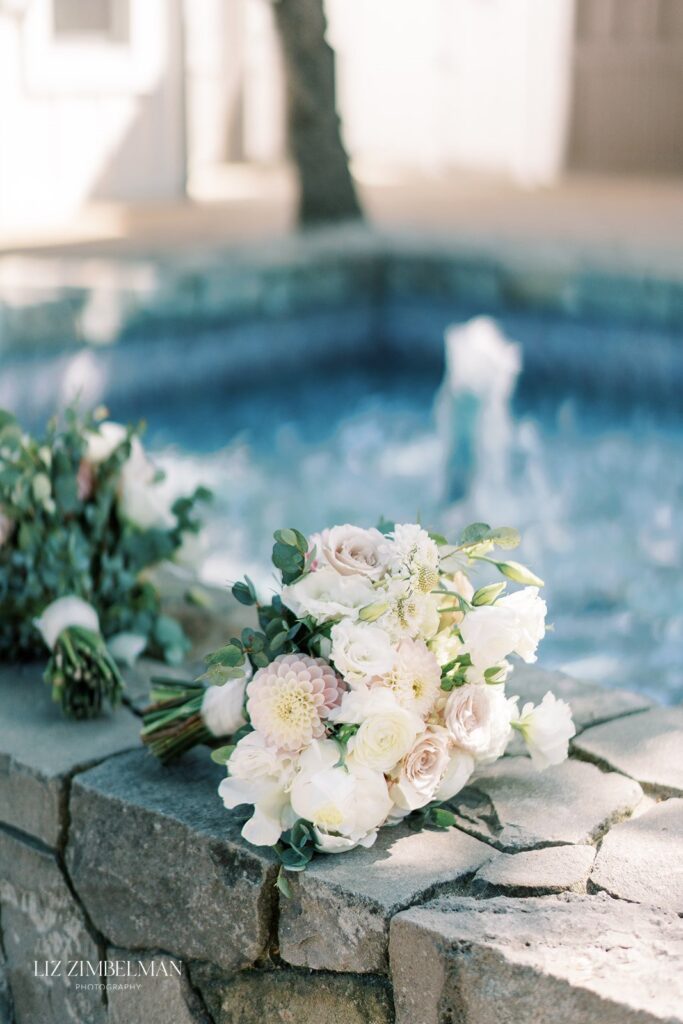 Bouquet of white and pale pink flowers resting on a stone ledge by a fountain.
