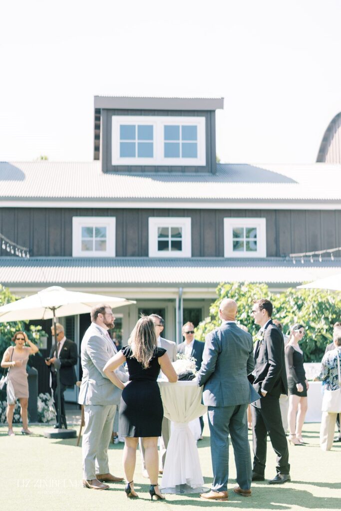 A group of people in formal attire stand and talk outside in front of a large building with multiple windows.