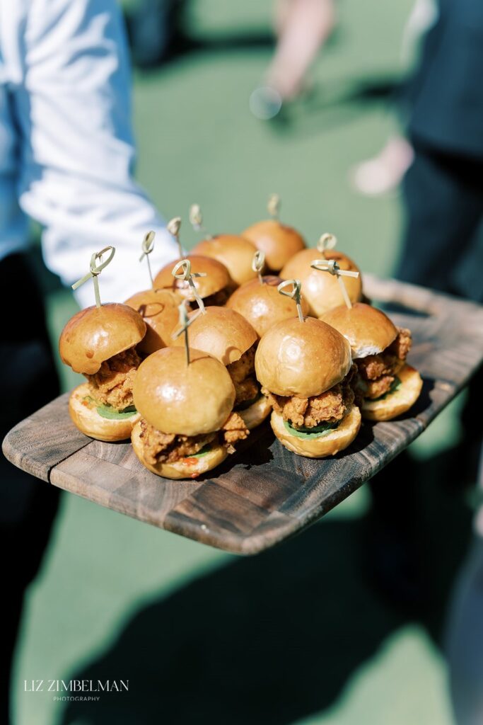 A tray of mini chicken sandwiches with toothpicks is being served outdoors.