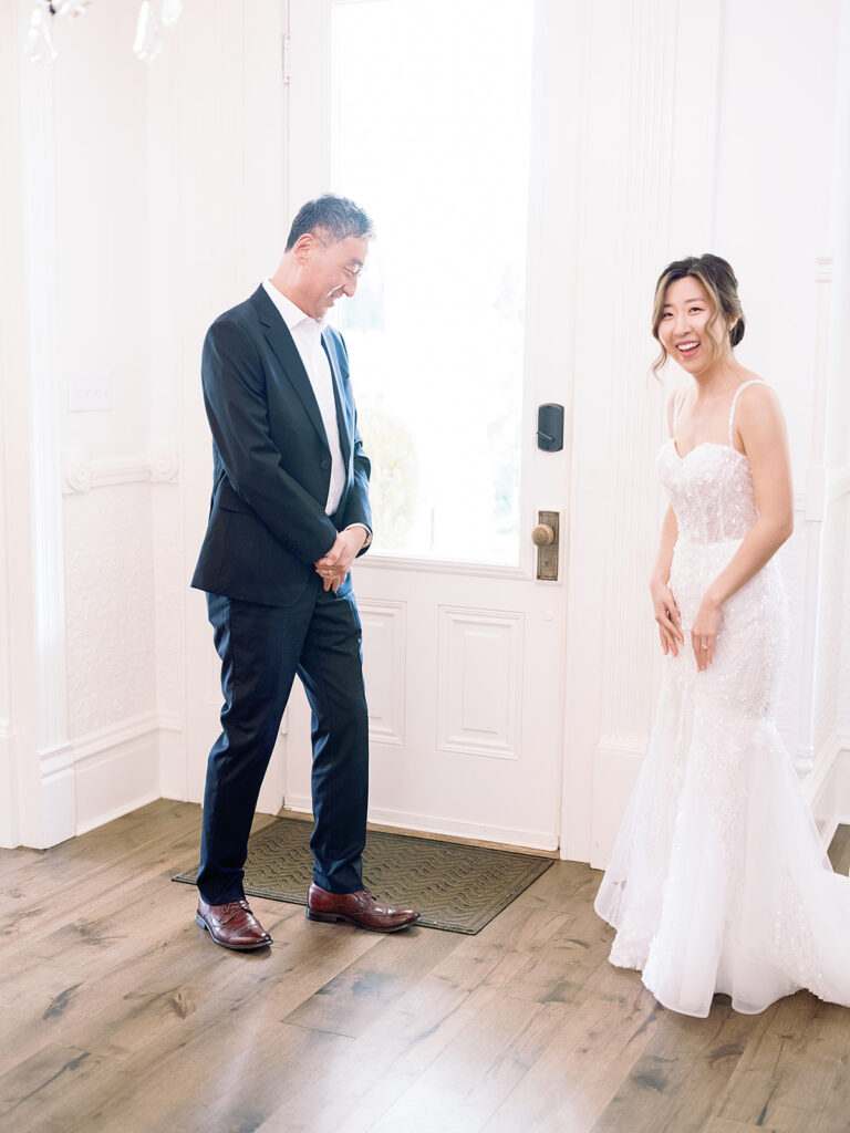 A person in a suit gazes at someone in a white dress inside a room with wooden floors and a closed door, reminiscent of the enchanting ambiance found at Park Winters weddings.