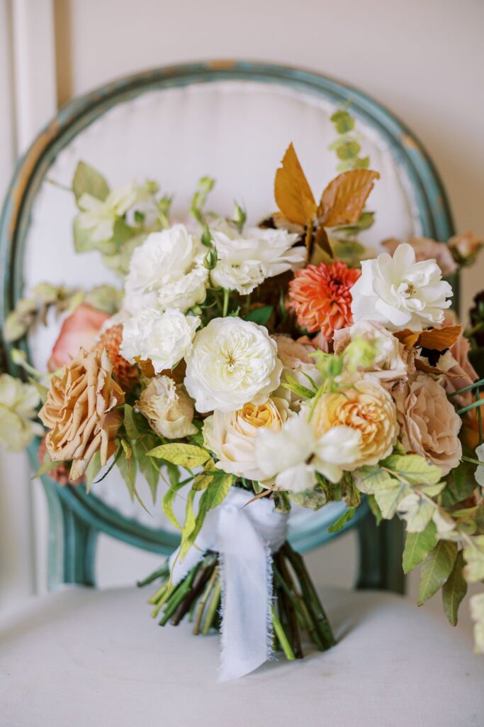 A bouquet of assorted flowers, including white and peach roses, sits on a teal chair with a white cushion.