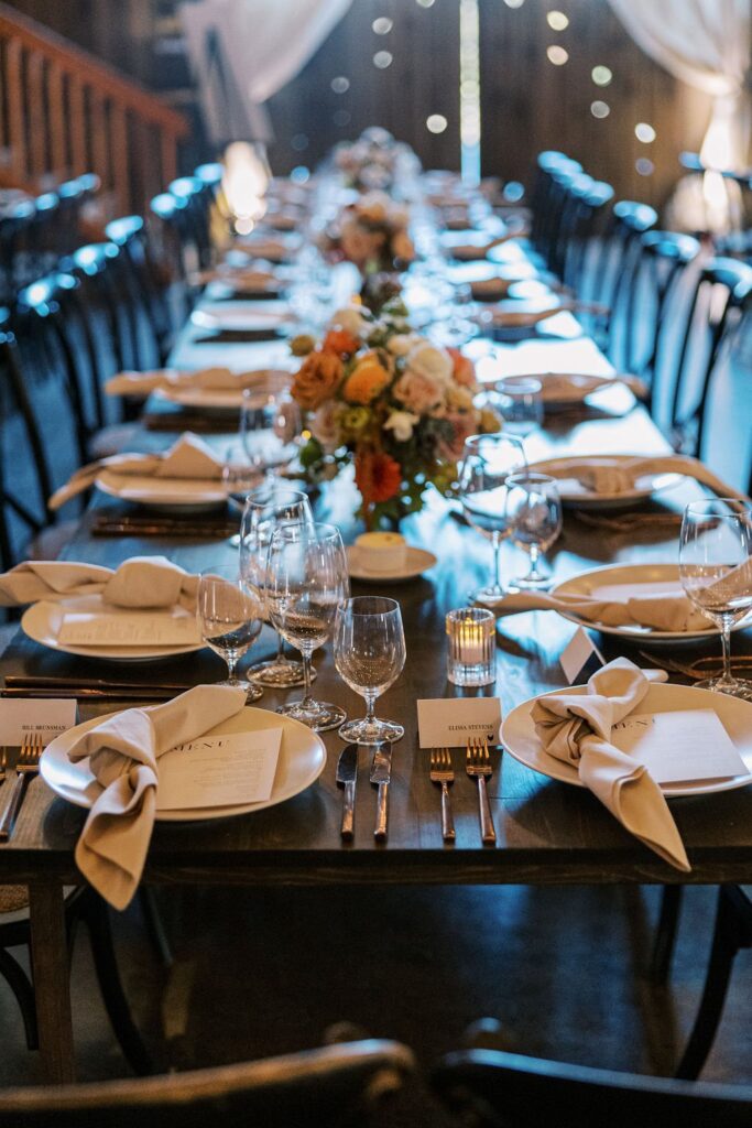 A long dining table set with plates, glasses, cutlery, and folded napkins. Floral centerpieces line the middle of the table.