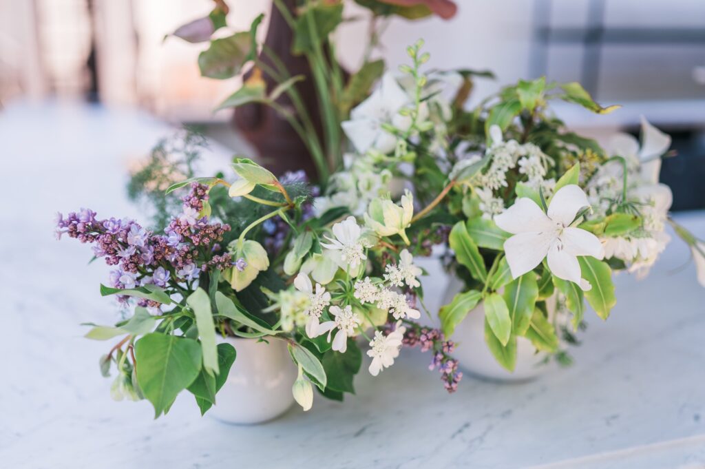 A floral arrangement featuring white and purple flowers with green leaves on a light marble surface.
