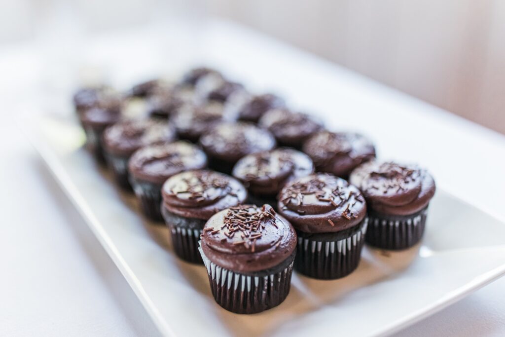 A tray of chocolate cupcakes with sprinkles arranged neatly on a white surface.