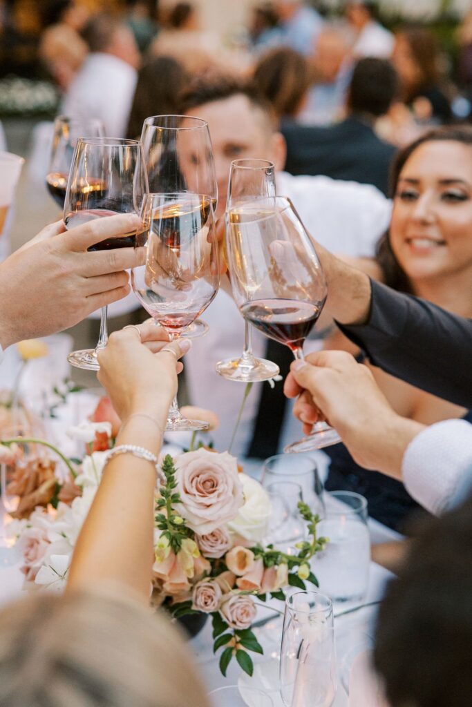 People clinking wine glasses at a table adorned with flowers and candles during a celebration.