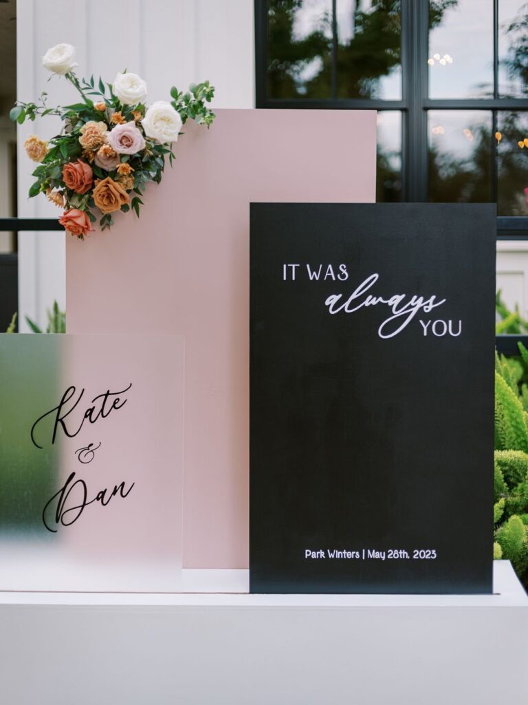 Wedding signage with floral arrangement. Text reads: "Kate & Dan" and "It was always you," dated "Park Winters | May 26th, 2023.