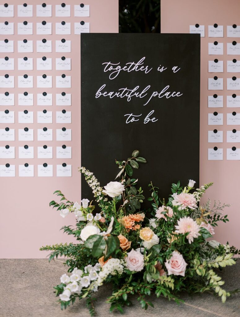 A black sign reads "together is a beautiful place to be," surrounded by pink card displays and floral arrangements.