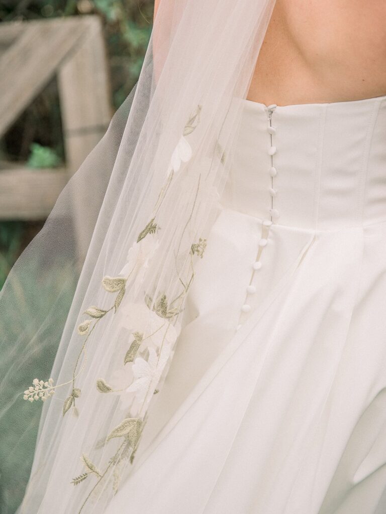 Close-up of a white wedding dress with floral embroidery on the veil and a row of buttons down the back.