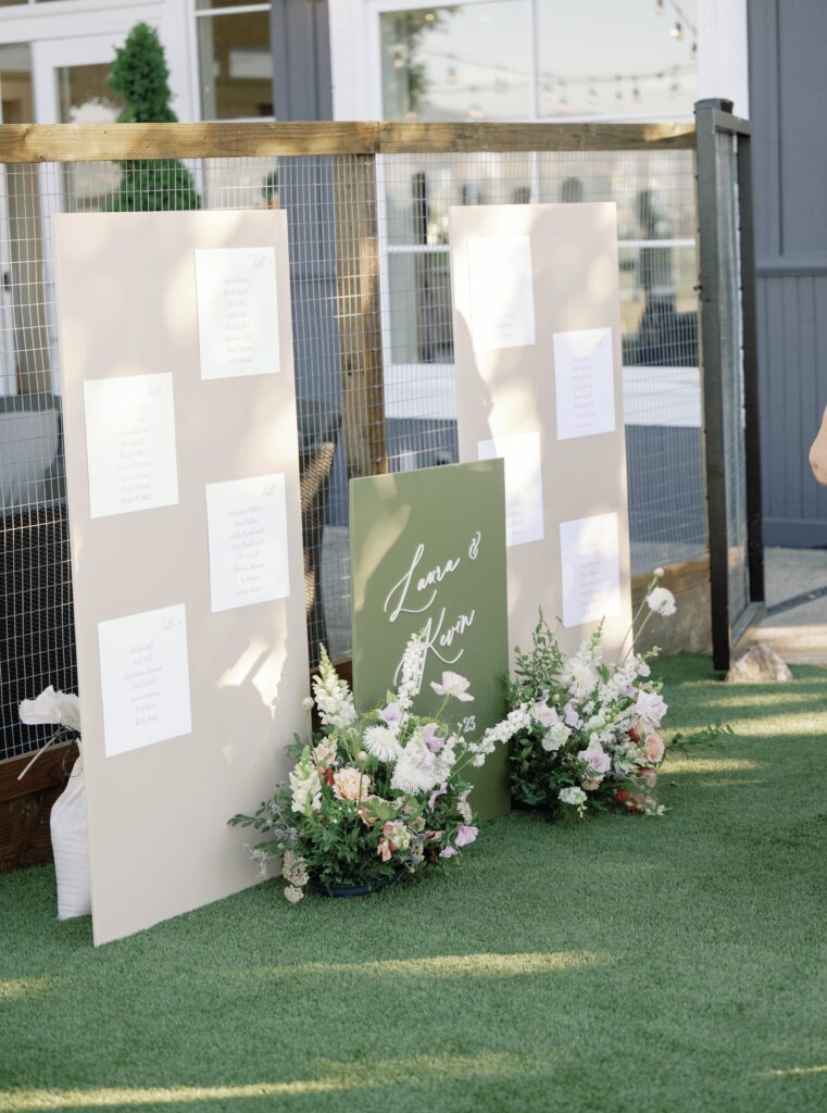 Seating charts and a welcome sign with floral arrangements are displayed on a lawn.